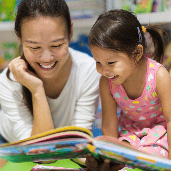 Young child joyfully reading a book with a parent, surrounded by colorful bookshelves, promoting a love for reading.