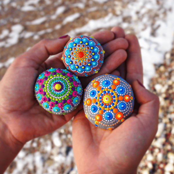 Children engaged in outdoor play, painting colorful rocks in a natural setting